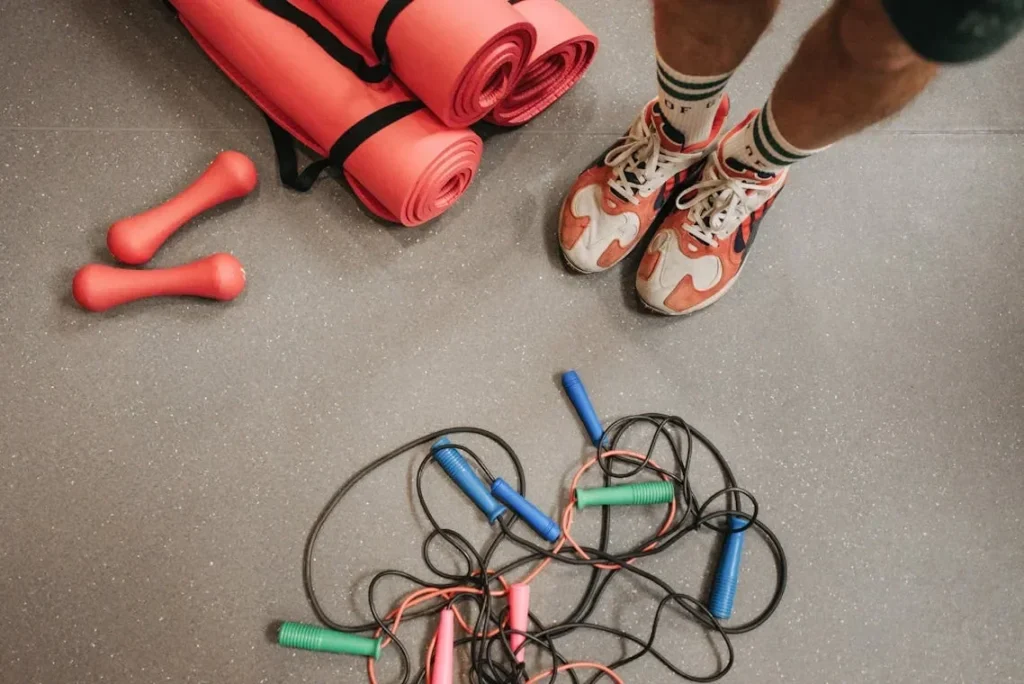 Fitness equipment including shoes, mats, weights, and skipping ropes on a gym floor.