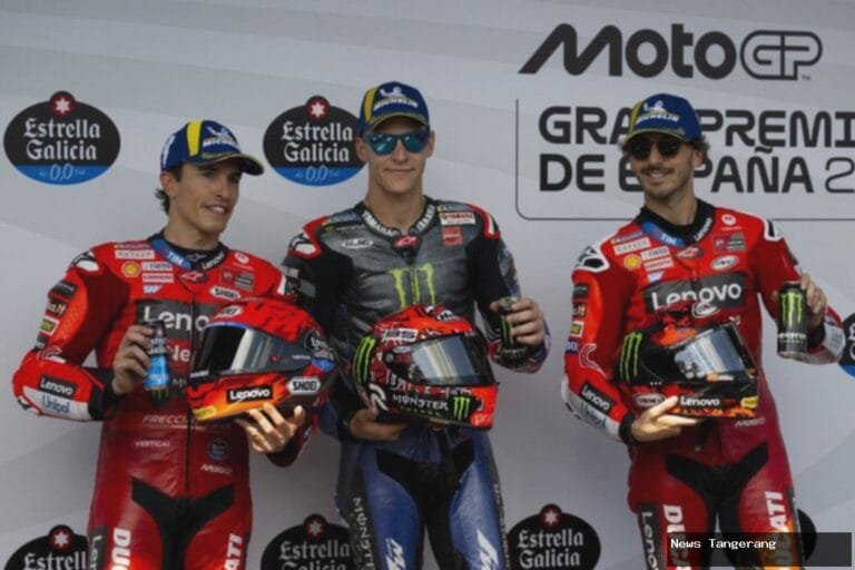 Tiga pembalap MotoGP di podium, memegang helm dan minuman energi.