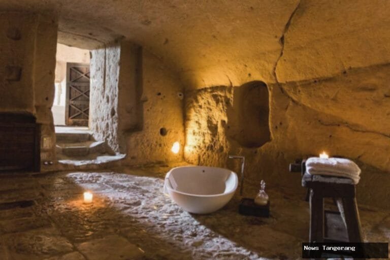 Kamar mandi mewah di dalam gua, dengan bathtub putih dan pencahayaan lilin.