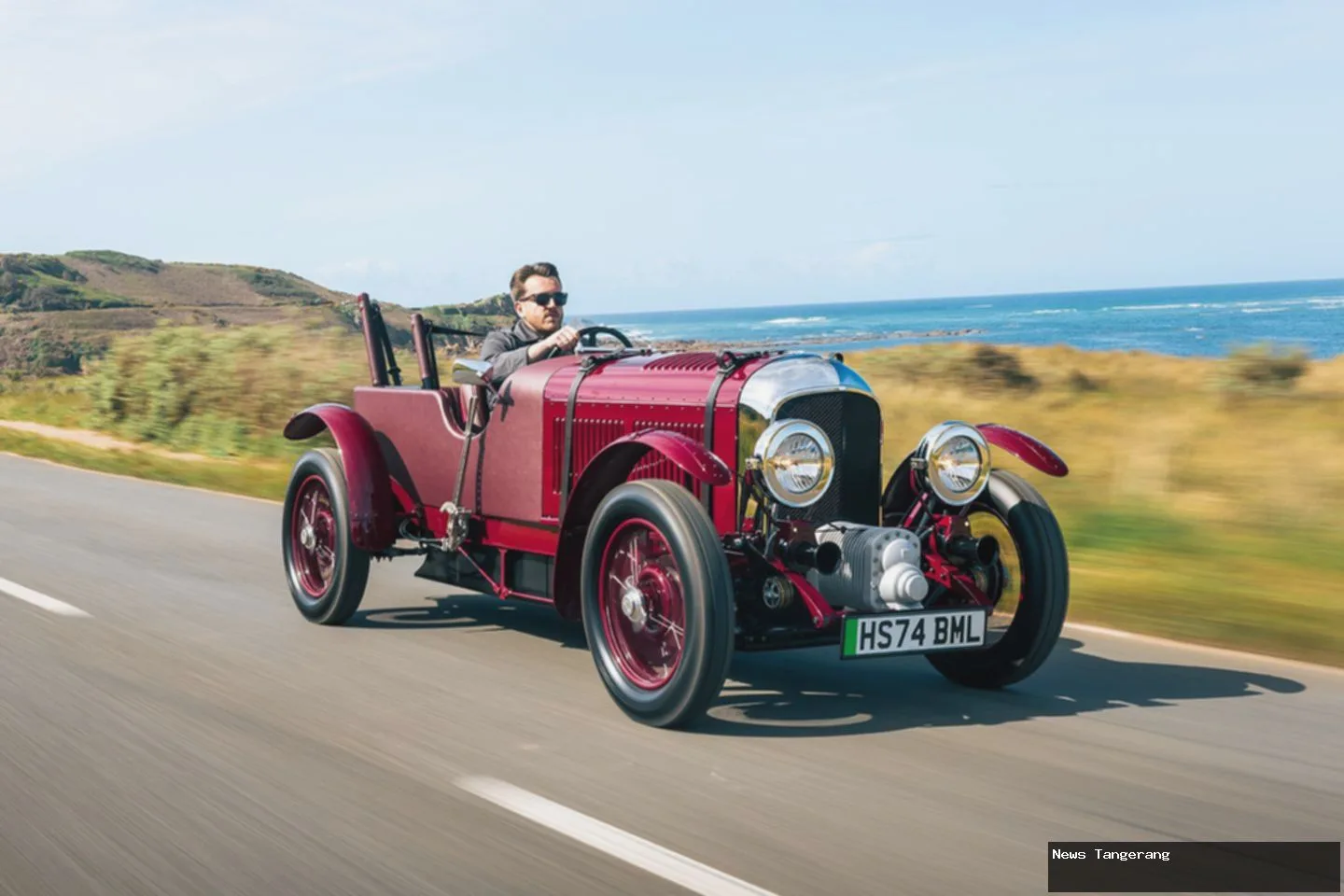 Bentley Blower Junior merah melaju di jalan tepi pantai, terinspirasi Blower Bentley 1929.