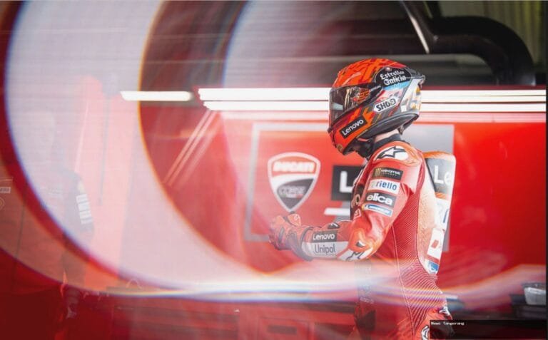 Pembalap MotoGP berseragam Ducati berwarna merah di garasi tim, fokus dan siap.
