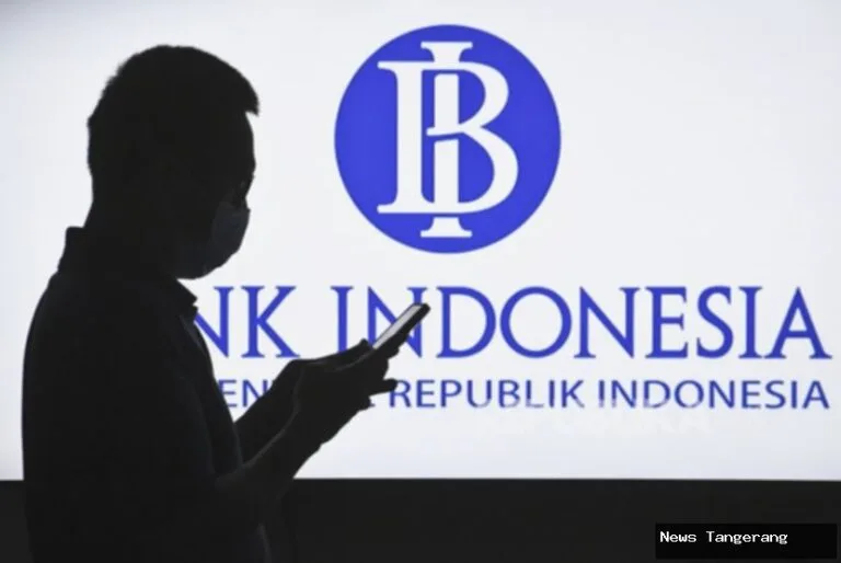 Siluet orang memegang ponsel di depan logo Bank Indonesia.