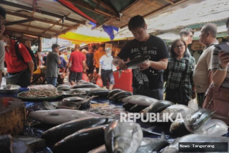 Suasana pasar tradisional dengan pembeli memilih ikan segar di meja pedagang.