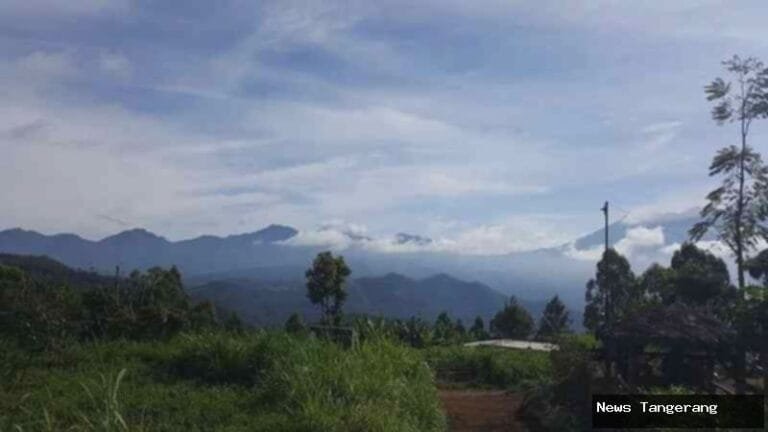 Pemandangan deretan gunung dari ketinggian, langit berawan, rerumputan hijau di depan.
