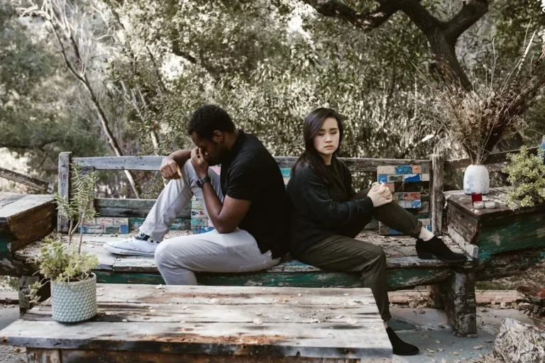 A couple sits back to back on a wooden bench, indicating a disagreement or breakup.
