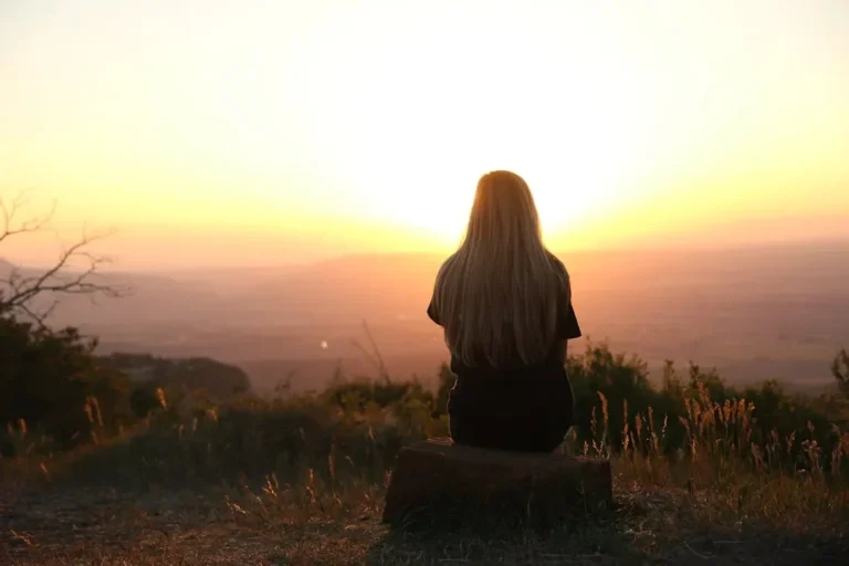 Woman sitting in nature, watching sunset over fields. Peaceful and serene outdoor scene.