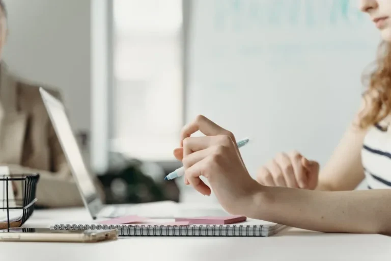 Close-up of a woman in an office, planning on a laptop with notes and pen.