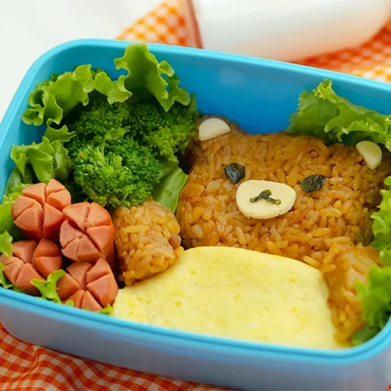 Bekal sekolah nasi goreng bentuk beruang, sosis, brokoli, telur dadar dalam kotak biru.