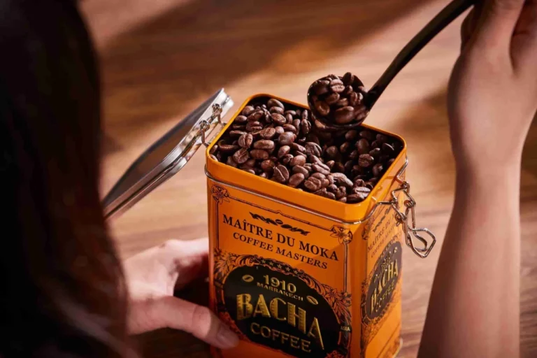 Biji kopi premium Bacha Coffee dalam kaleng oranye, disendok dengan sendok perak.