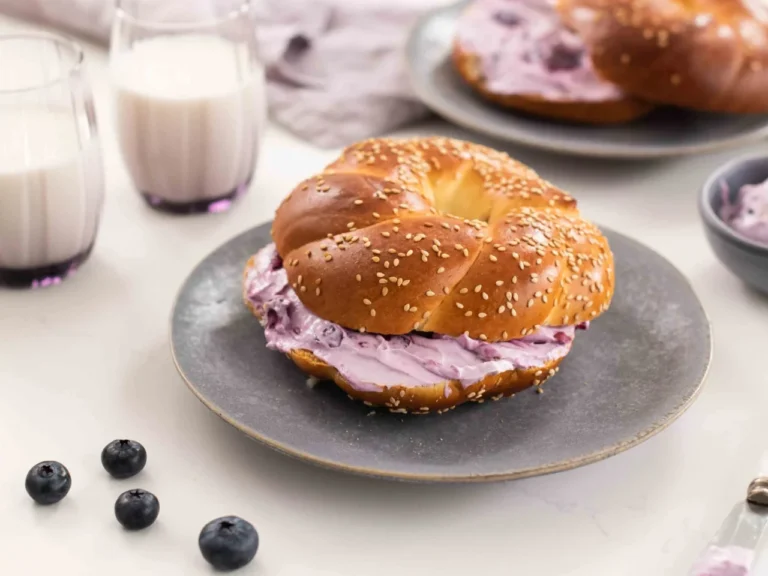 Bagel dengan isian krim blueberry, taburan wijen, di atas piring abu-abu.