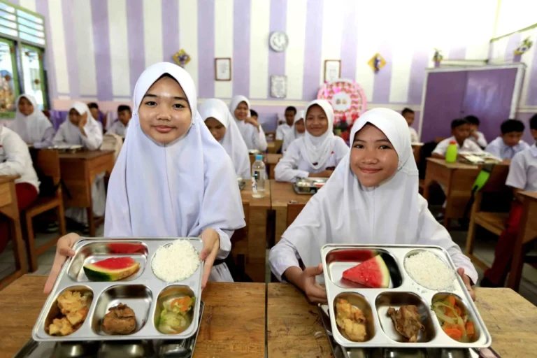 Dua siswi tersenyum bahagia menunjukkan menu Program Makan Bergizi Gratis di sekolah.
