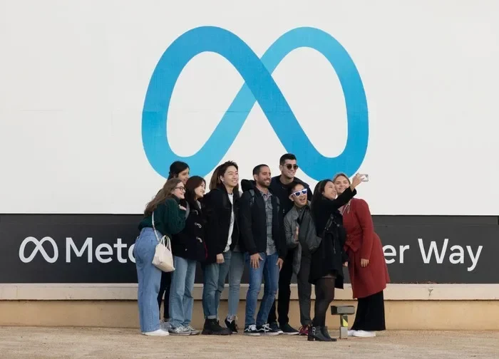 Sekelompok orang berswafoto di depan logo Meta Platforms, raksasa media sosial.