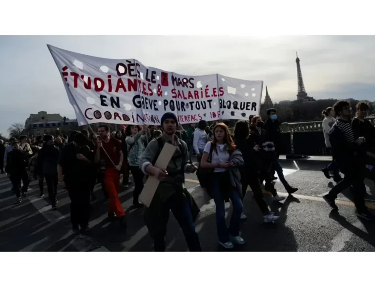 Sekelompok orang berdemonstrasi di jalan dengan spanduk di depan Menara Eiffel.