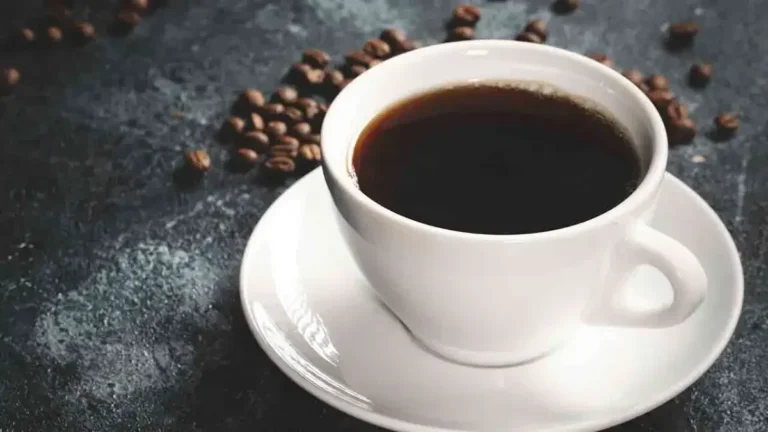 Secangkir kopi hitam dan biji kopi di atas meja gelap.