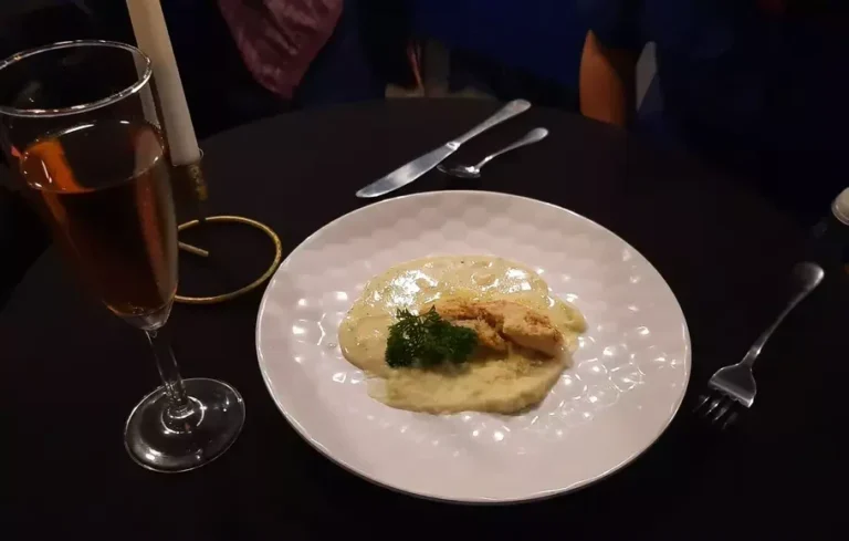 Hidangan fine dining dengan porsi kecil, minuman, lilin di atas meja hitam.