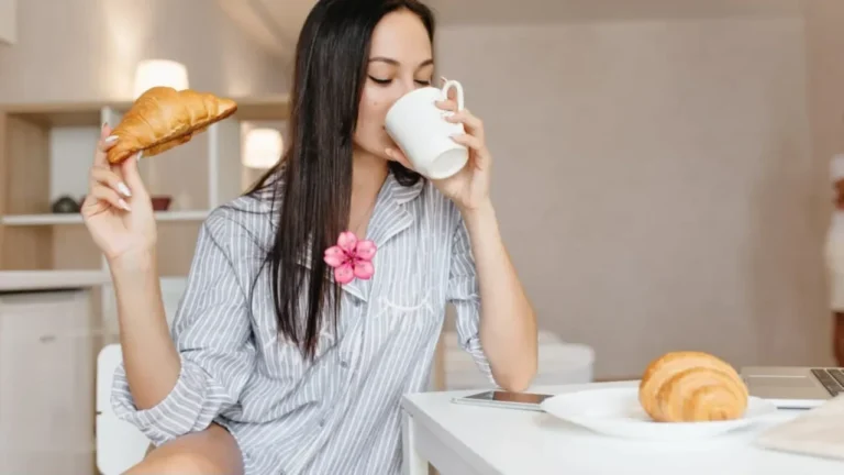 Wanita menikmati kopi dan croissant di meja, fokus, energi setelah makan.