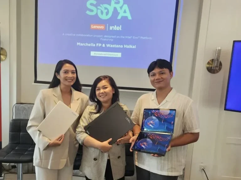 Tiga orang memegang laptop Lenovo di depan layar presentasi acara kolaborasi.