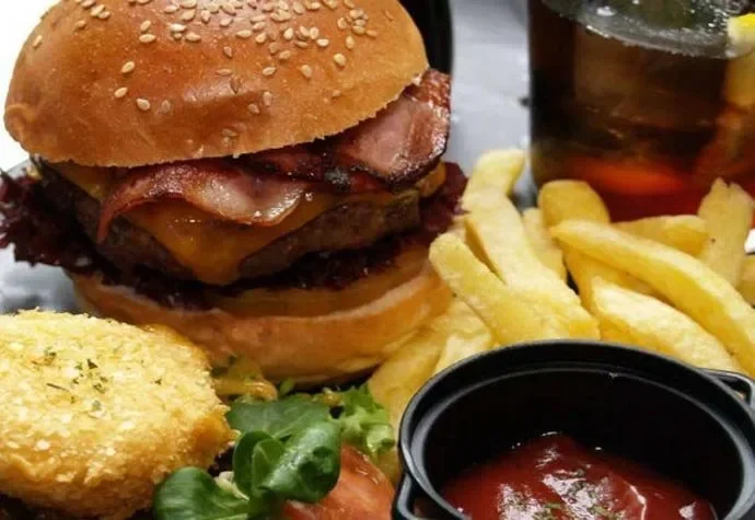 Burger dengan daging asap, keju, kentang goreng, dan saus tomat.