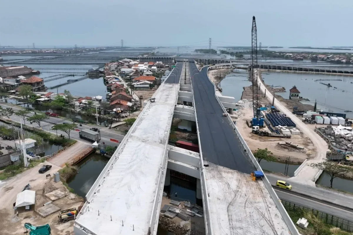 Pemandangan jalan tol yang sedang dibangun, jembatan, dan pemukiman di sekitarnya.