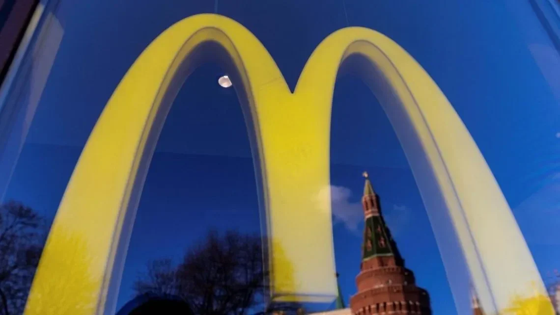 Logo McDonald's terpantul di jendela, dengan bayangan bangunan khas Rusia.