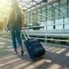 A woman walks with a suitcase outside an airport terminal, ready for travel.