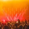 Energetic crowd at a live concert with bright stage lights and hands raised in celebration.