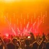 Energetic crowd at a live concert with bright stage lights and hands raised in celebration.