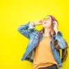 Smiling woman in sunglasses stands against vibrant yellow wall, radiating happiness.
