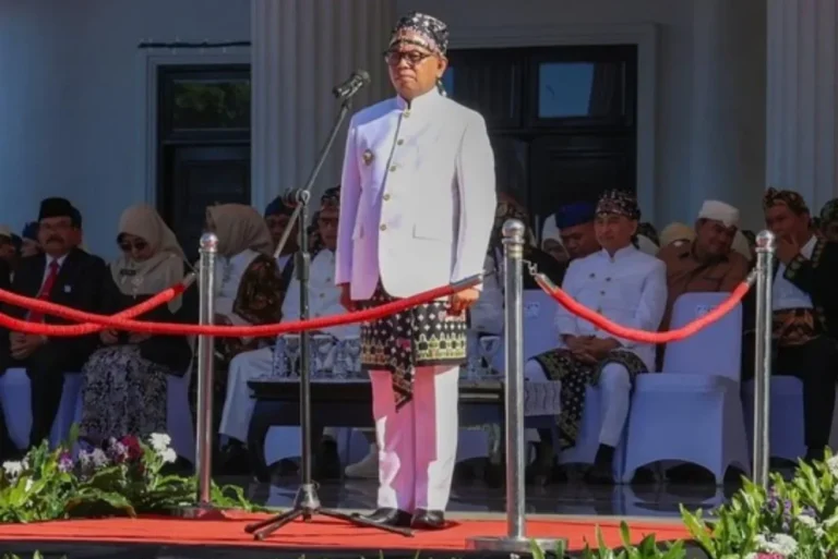 Gubernur Banten Andra Soni Mengenakan berbusana adat putih dan udeng berbicara di mimbar, hadirin menyaksikan.