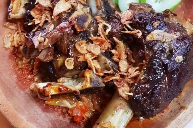 Potongan iga bakar berlumur bumbu kecokelatan dengan taburan bawang goreng di piring kayu.