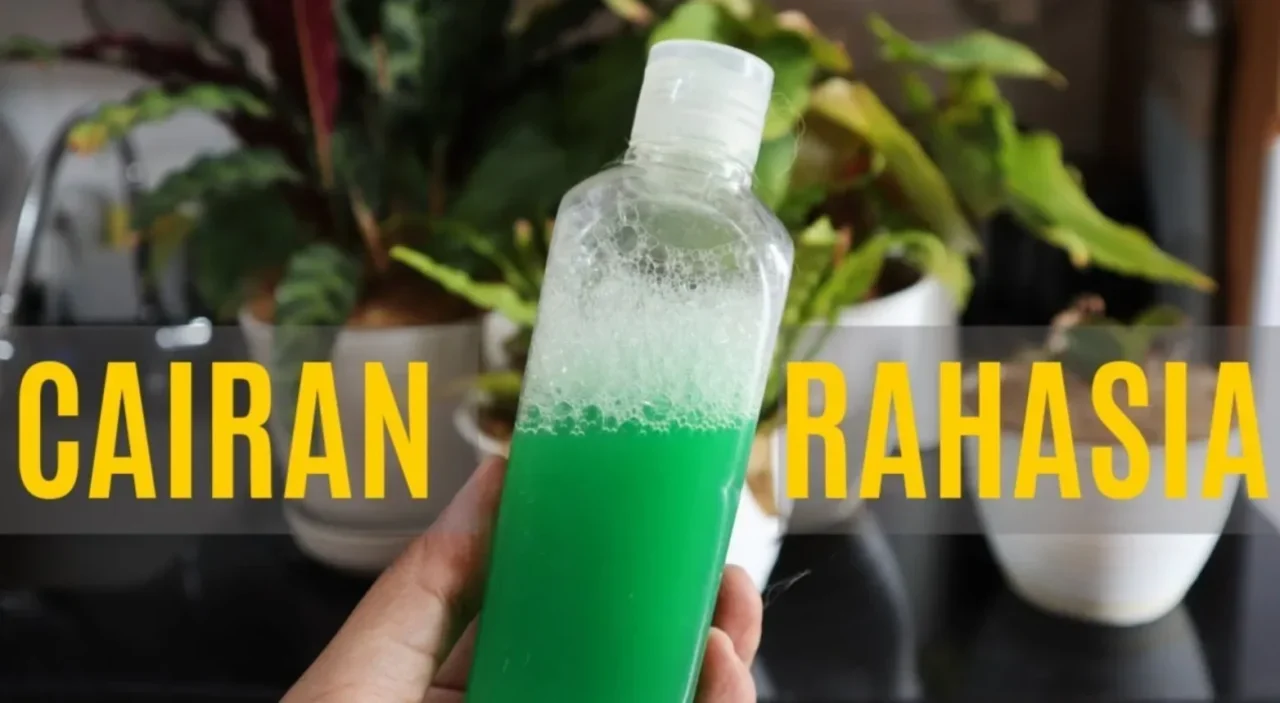 Tangan memegang botol berisi cairan hijau berbusa, bertuliskan 'Cairan Rahasia' dengan latar tanaman hijau.