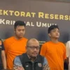 Konferensi pers polisi, menampilkan dua tersangka berbaju oranye di depan papan Direktorat Reserse Kriminal Umum.