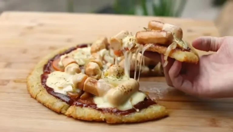 Tangan mengangkat sepotong pizza sosis keju dengan lelehan keju menggoda di atas talenan kayu.