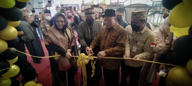 Dua tokoh memotong pita kuning dalam acara peresmian, disaksikan hadirin dan dekorasi balon.