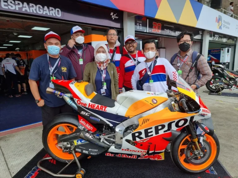 Sekelompok orang berpose di samping motor balap MotoGP Repsol Honda di area pit.