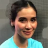 Potret wanita tersenyum ramah dengan rambut terikat dan mengenakan kaus biru.