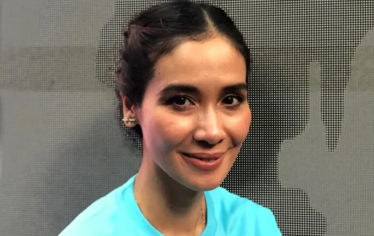 Potret wanita tersenyum ramah dengan rambut terikat dan mengenakan kaus biru.