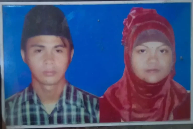 Foto formal dua individu, seorang pria berpeci dan wanita berhijab merah, berlatar biru.