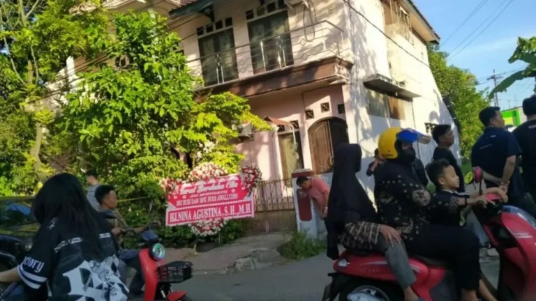 Karangan bunga duka cita di depan rumah Hj. Nina Agustina, dengan warga sekitar berkumpul.