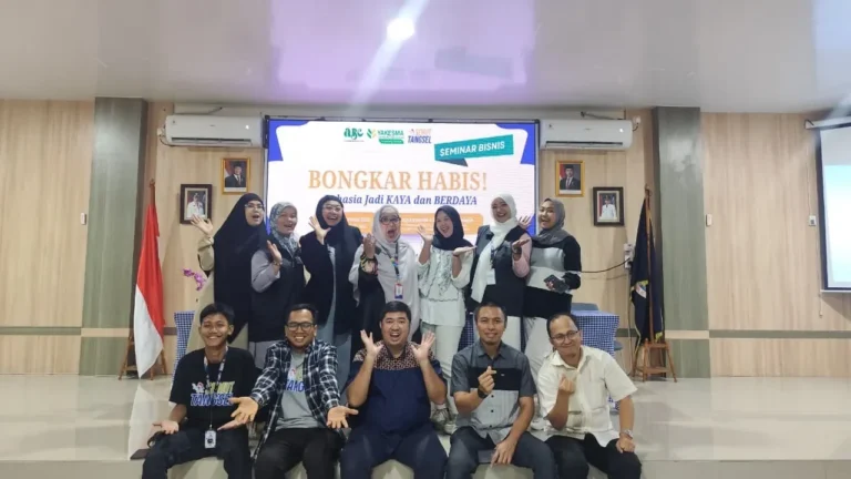 Panitia acara seminar bisnis "Bongkar Habis!" berpose ceria di depan panggung dengan spanduk acara.