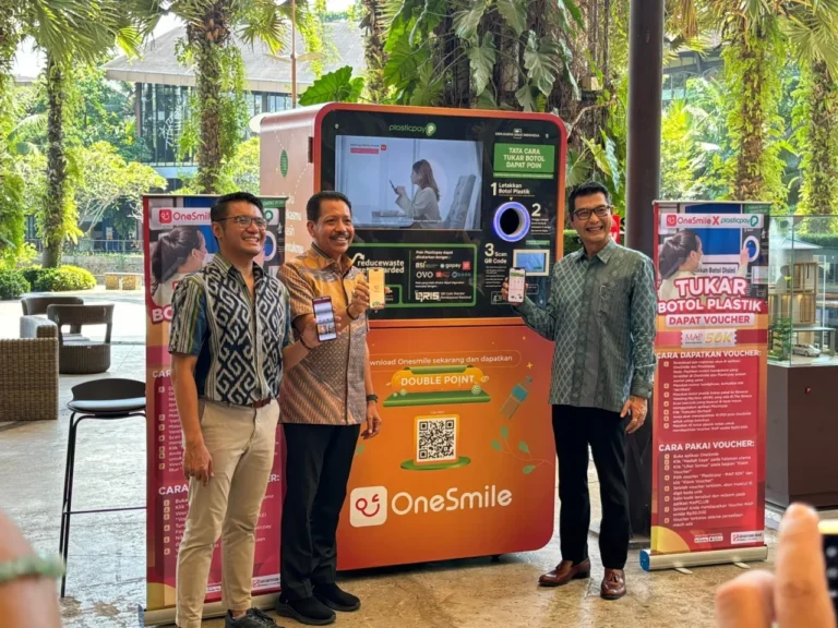 Tiga pria tersenyum di depan RVM Plasticpay dan OneSmile, inovasi daur ulang botol plastik.