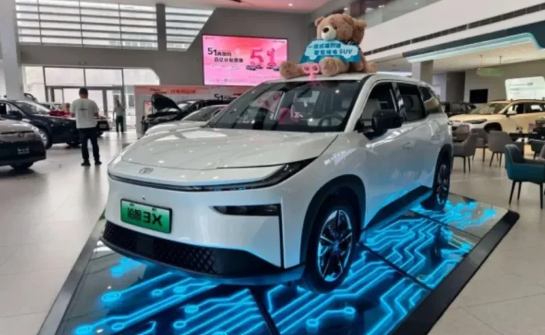 Mobil SUV listrik putih futuristik dipajang di showroom dengan pencahayaan sirkuit biru.