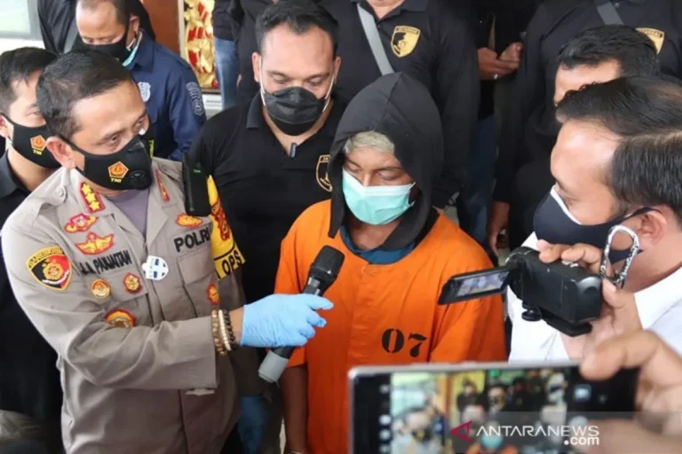 Polisi mewawancarai tersangka berbaju oranye dan bermasker dalam konferensi pers yang direkam media.