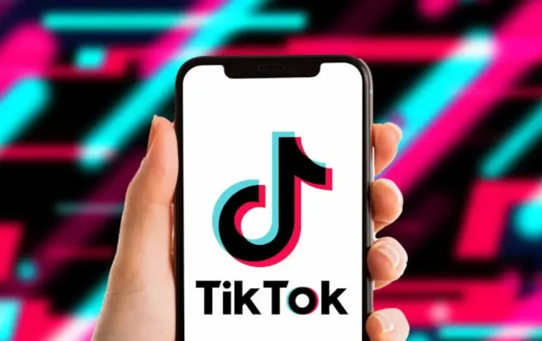 Tangan memegang ponsel menampilkan logo aplikasi TikTok dengan latar belakang neon.