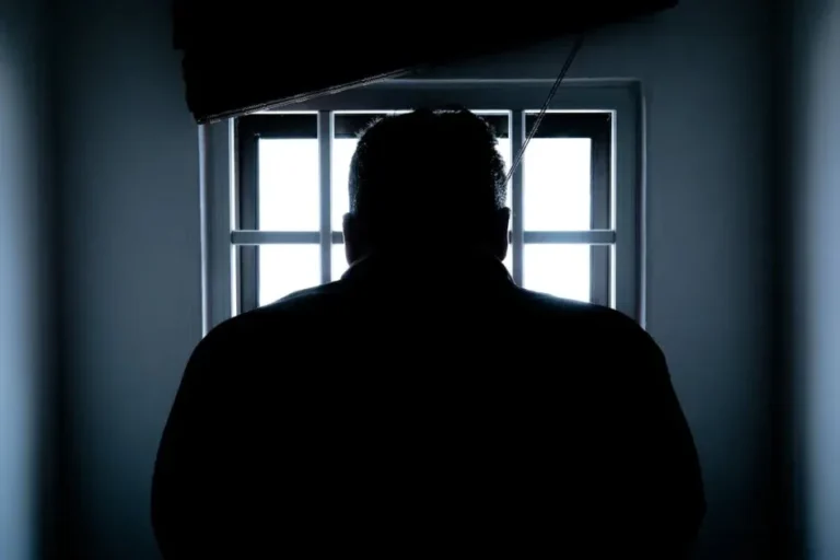 Dark silhouette of a man in a prison cell, backlit by window bars.