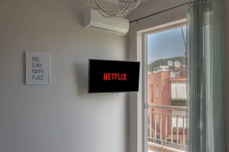 A comfortable room with Netflix on TV and window view of outside buildings.