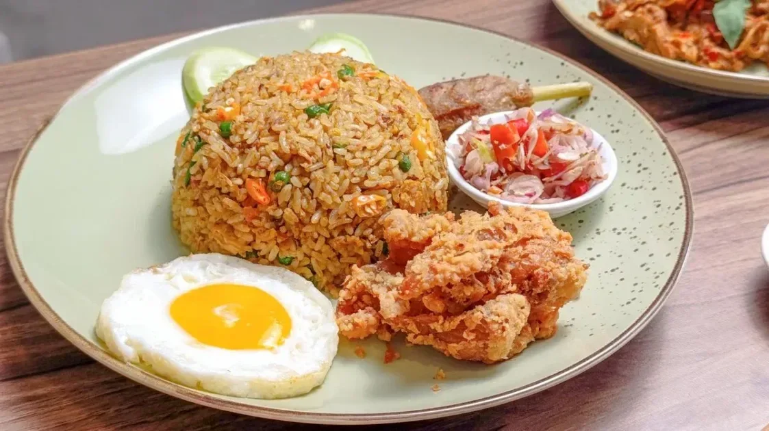 Tasty Asian fried rice dish with fried egg, fried chicken, and fresh vegetables on a plate.