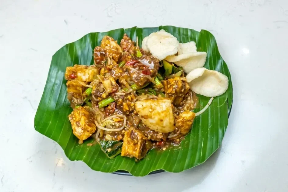 Top view of Indonesian Gado-Gado salad on a banana leaf with spicy peanut sauce and crackers.
